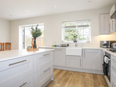 A kitchen with white cabinets a wooden floor a window above the sink and a kitchen island at Iscoed in Llangefni