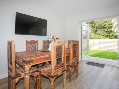 A dining room with wooden table and chairs a vase with flowers on the table a wall-mounted television and open doors leading to a garden at Iscoed in Llangefni