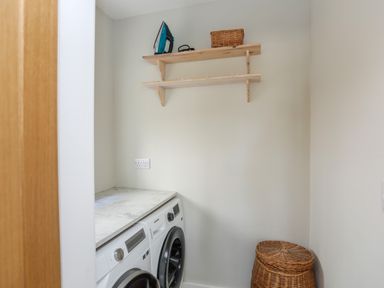 A laundry room with a washing machine dryer wicker basket and wooden shelves at Iscoed in Llangefni