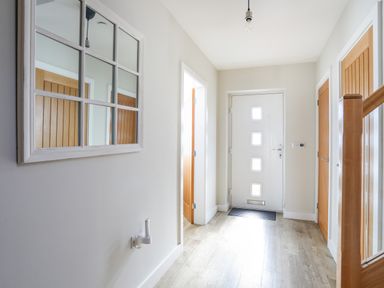 A hallway with a white front door and wooden interior doors at Iscoed in Llangefni