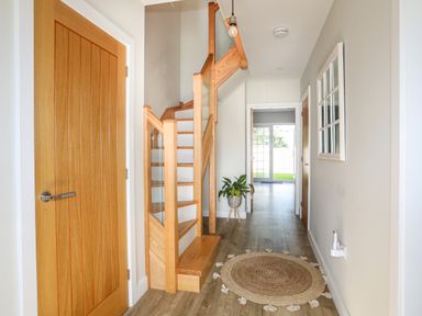 A hallway with wooden stairs and doors a round woven rug and a plant at Iscoed in Llangefni