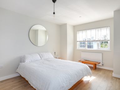 A bedroom with a bed and white bedding a round mirror on the wall and a wooden bench under a window at Iscoed in Llangefni
