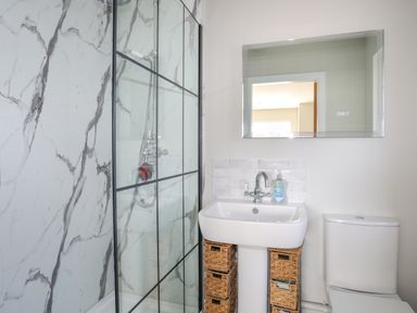 A bathroom with a shower area with a glass door sink with storage baskets below and a toilet at Iscoed in Llangefni