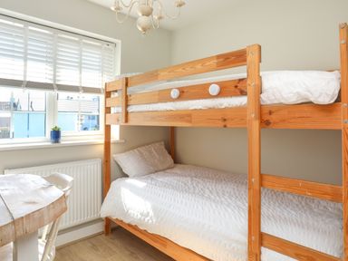 A bedroom with wooden bunk beds and a table near a window with blinds at Iscoed in Llangefni
