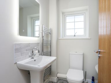 A bathroom with a sink mirror window toilet and towel rack at Iscoed in Llangefni
