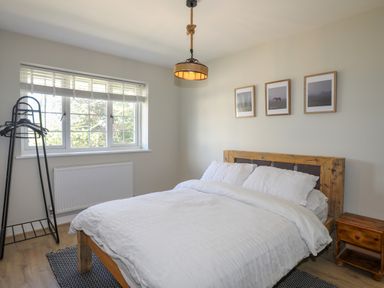 A bedroom with a wooden bed and white bedding a wooden nightstand a black standing hanger near a window and three framed pictures on the wall at Iscoed in Llangefni