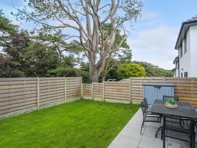 A fenced backyard with green grass a large tree a patio area with a table and chairs and a storage box at Iscoed in Llangefni