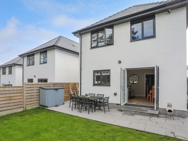 A backyard with a patio table and chairs a storage shed and open double doors leading inside at Iscoed Llangefni