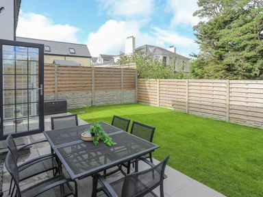 A backyard with a metal table and chairs set on a patio next to a grassy lawn and wooden fence at Iscoed in Llangefni
