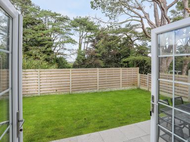 A garden with green grass and wooden fence viewed through open glass doors at Iscoed in Llangefni