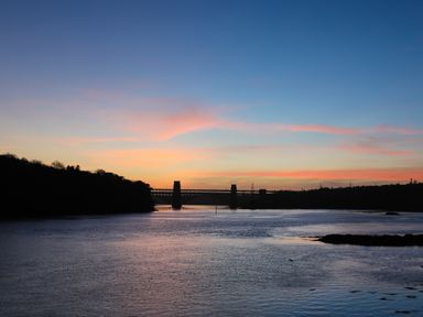 A body of water with a bridge and trees at sunset at Iscoed in Llangefni