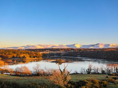 A river with a bridge over it trees on the riverbanks and snow covered mountains in the background at Iscoed in Llangefni