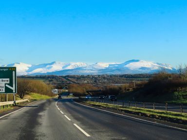 A highway with cars and road signs with snow covered mountains in the background at Iscoed in Llangefni