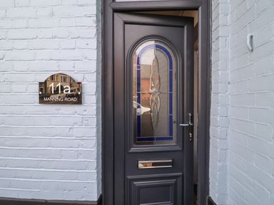 A black door with patterned glass and a silver handle on a white brick wall with a 11a Manning Road house number plaque next to it at 11a Manning Road Felixstowe Suffolk