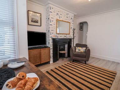 A living room with a striped rug armchair fireplace television and pastries on a table at 11a Manning Road Felixstowe Suffolk