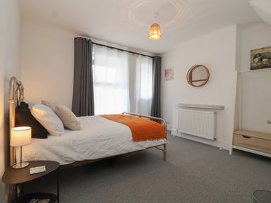 A bedroom with a metal bed frame an orange throw on the bed curtains on the window and a round mirror on the wall at 11a Manning Road in Felixstowe Suffolk