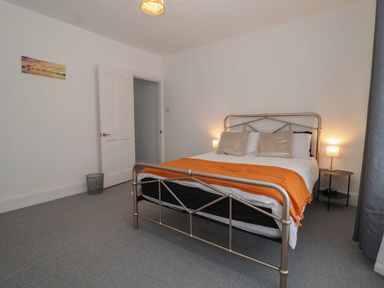 A bedroom with a metal bed frame, orange blanket on the bed, two bedside tables with lamps and a painting on the wall at 11a Manning Road in Felixstowe Suffolk