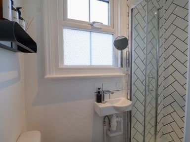 A small bathroom with a sink, a window with patterned glass, a shower with herringbone tiled walls, and a shelf with bottles at 11a Manning Road in Felixstowe Suffolk