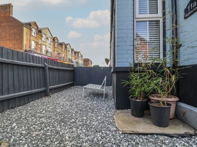 A fenced gravel yard with a white bench and potted plants outside a blue and black house at 11a Manning Road in Felixstowe Suffolk