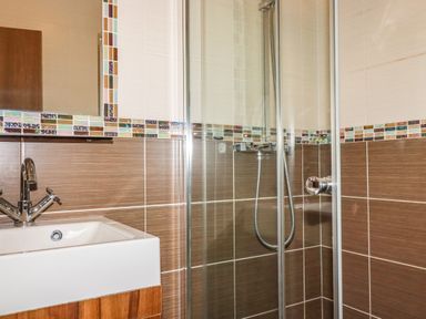 A bathroom with a sink and faucet next to a glass shower enclosure with a handheld showerhead at Hideaway Lodge in Bossiney near Tintagel