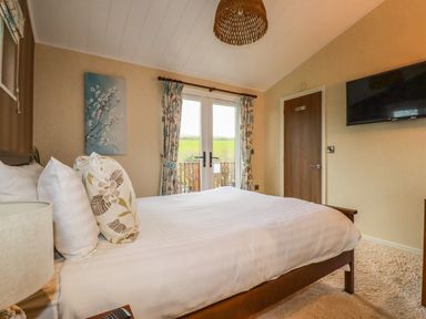 A bedroom with a double bed pillows curtains and a wall mounted tv at Hideaway Lodge in Bossiney near Tintagel