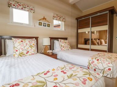 A bedroom with two single beds floral pillows and blankets a bedside table with a lamp and a wardrobe with mirrored sliding doors at Hideaway Lodge in Bossiney near Tintagel