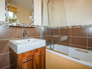 A bathroom with a sink cabinet a bathtub shower and a mirror with a small plant at Hideaway Lodge Bossiney near Tintagel