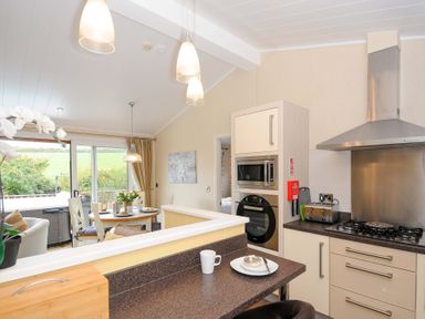A kitchen with a breakfast bar dining table and chairs and large window at Hideaway Lodge in Bossiney near Tintagel