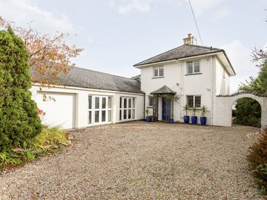 A white two-story house with multiple blue pots with plants on a gravel driveway at Bwthyn in Borth-y-Gest near Porthmadog