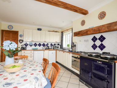 A kitchen with white cabinets a blue range cooker a dining table with chairs and flowers at Bwthyn in Borth-y-Gest near Porthmadog