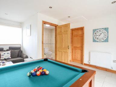 A pool table with balls set up in a room with two wooden doors a gray sofa and a clock on the wall at Bwthyn in Borth-y-Gest near Porthmadog