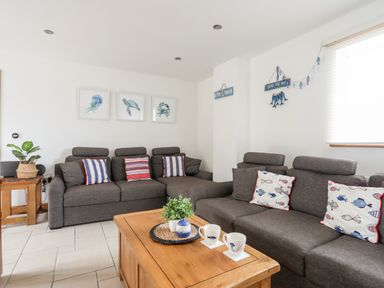 A living room with grey sofas and striped and fish patterned cushions at Bwthyn in Borth-y-Gest near Porthmadog