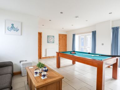 A room with a pool table coffee table two mugs a plant clock on the wall and blue curtains at Bwthyn in Borth-y-Gest near Porthmadog