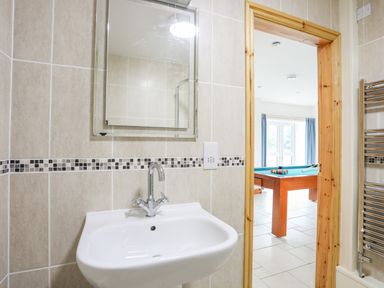 A bathroom with a sink mirror and tiled walls looking into a room with a pool table at Bwthyn in Borth-y-Gest near Porthmadog
