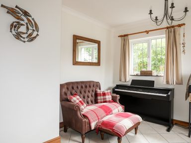 A room with a brown leather armchair and ottoman covered with red plaid blankets and pillows next to a black digital piano under a window at Bwthyn in Borth-y-Gest near Porthmadog