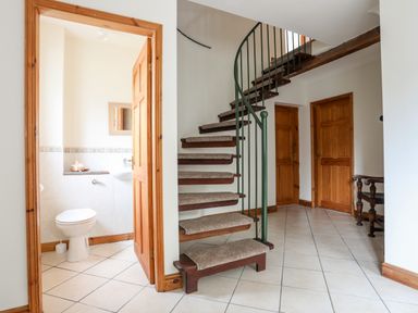 A hallway with a spiral staircase and tiled floor with wooden doors and a small bathroom at Bwthyn in Borth-y-Gest near Porthmadog