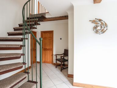 A hallway with a spiral staircase a wooden chair and wooden doors at Bwthyn in Borth-y-Gest near Porthmadog