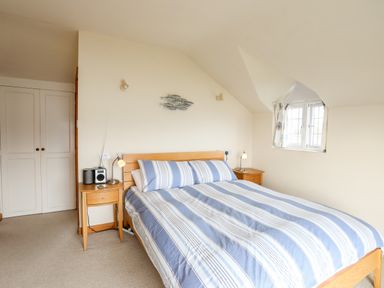 A bedroom with a double bed with striped linens two wooden bedside tables and a window at Bwthyn in Borth-y-Gest near Porthmadog