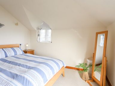 A bedroom with a double bed striped bedding nightstand lamp window standing mirror and plant at Bwthyn in Borth-y-Gest near Porthmadog