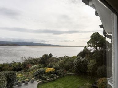 A garden with shrubs and a lawn overlooking a large body of water with hills in the background at Bwthyn in Borth-y-Gest near Porthmadog