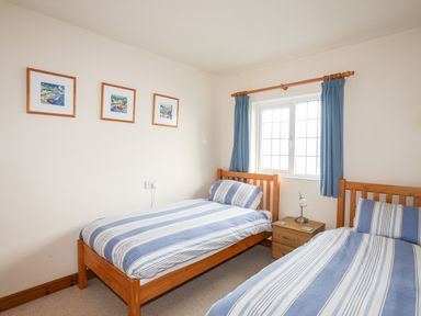 A bedroom with two single beds with striped bedding a window with blue curtains and three framed pictures on the wall at Bwthyn in Borth-y-Gest near Porthmadog