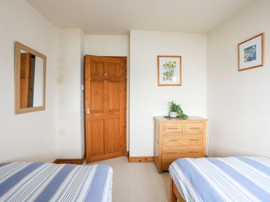 A bedroom with two single beds with striped bedding a wooden dresser a wooden door and two framed pictures at Bwthyn in Borth-y-Gest near Porthmadog