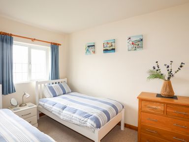 A bedroom with two single beds a wooden chest of drawers with a vase and blue curtains at Bwthyn in Borth-y-Gest near Porthmadog