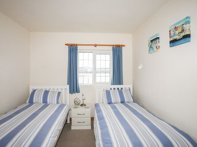 A bedroom with two single beds a nightstand between them with a lamp and mirror a window with blue curtains and paintings on the wall at Bwthyn in Borth-y-Gest near Porthmadog