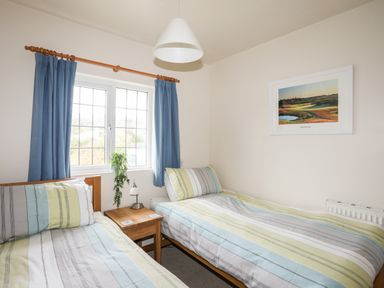 A bedroom with two single beds a wooden nightstand between them a window with blue curtains and a framed picture on the wall at Bwthyn in Borth-y-Gest near Porthmadog