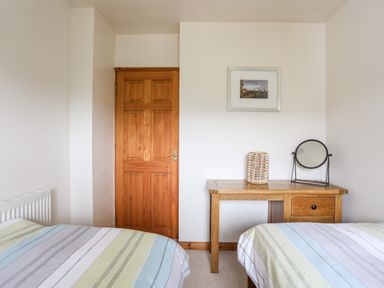 A bedroom with two beds striped bedding a wooden door a wooden desk with a round mirror and a decorative candle holder on it and a framed picture on the wall at Bwthyn in Borth-y-Gest near Porthmadog
