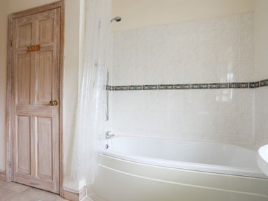 A bathroom with a bathtub shower wooden door and tiled walls at Bwthyn Borth-y-Gest near Porthmadog