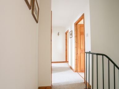 A hallway with carpet and wooden doors and frames with pictures on the walls at Bwthyn in Borth-y-Gest near Porthmadog