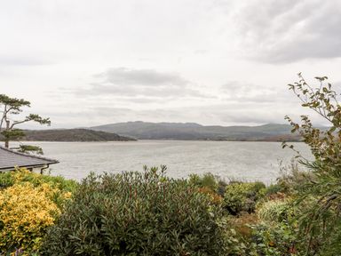 A view of a body of water with hills in the background and bushes in the foreground at Bwthyn in Borth-y-Gest near Porthmadog