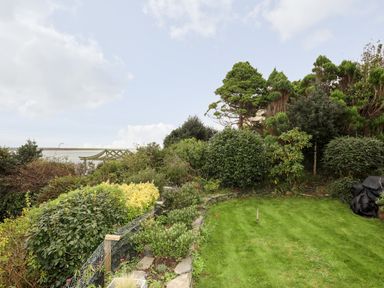 A garden with green grass lawn and various bushes and trees overlooking a body of water at Bwthyn in Borth-y-Gest near Porthmadog